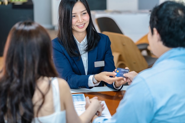 Saleswoman asiatica che riceve la carta di credito dal cliente della coppia quando la decisione compra la nuova automobile