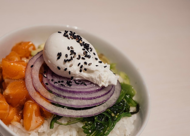 Asian salmon poke bowl With avocadochinese chives red onion wakame seaweed poached freerange egg sesame oil and kimchee on white background Tasty and diet food Top side view with copy space