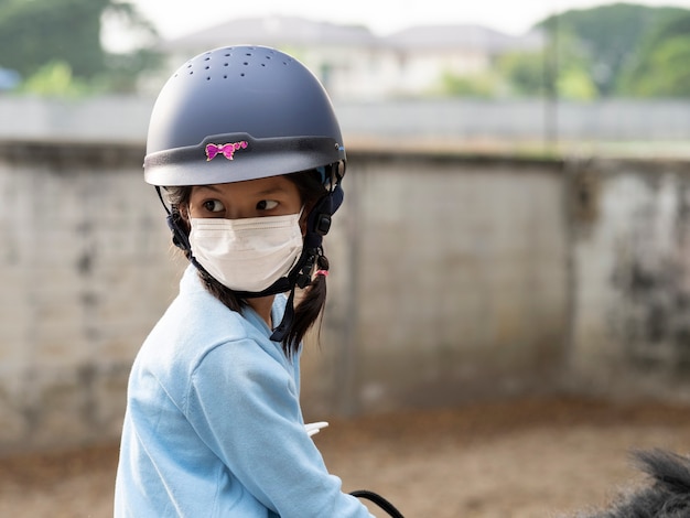 馬、乗馬、または馬の牧場での乗馬の練習をしているアジアの学校の子供の女の子。