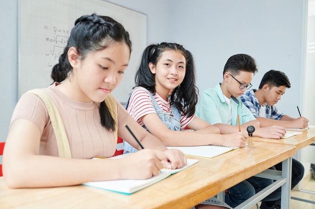 그녀의 급우가 수업 시간에 공부하고 카피 북에 쓰는 아시아 학교 학생