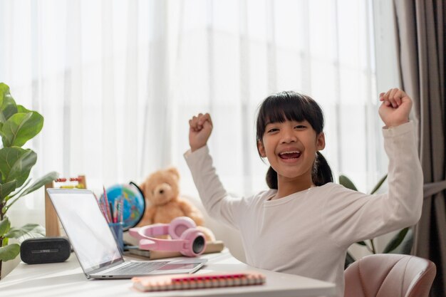  asian schoolgirl doing her homework with laptop at home children use gadgets to study education and distance learning for kids homeschooling during quarantine stay at home