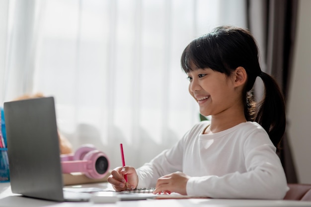 Asian schoolgirl doing her homework with laptop at home Children use gadgets to study Education and distance learning for kids Homeschooling during quarantine Stay at home