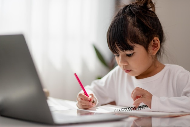 Asian schoolgirl doing her homework with laptop at home Children use gadgets to study Education and distance learning for kids Homeschooling during quarantine Stay at home