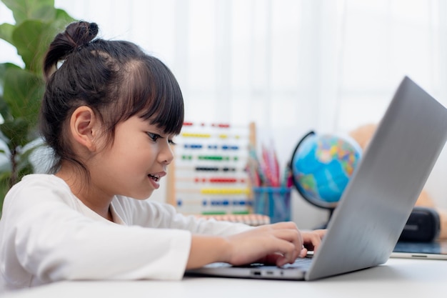 Asian schoolgirl doing her homework with laptop at home Children use gadgets to study Education and distance learning for kids Homeschooling during quarantine Stay at home