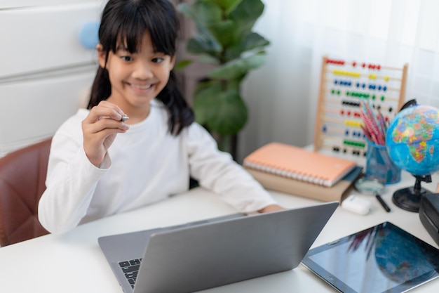 Asian schoolgirl doing her homework with laptop at home Children use gadgets to study Education and distance learning for kids Homeschooling during quarantine Stay at home