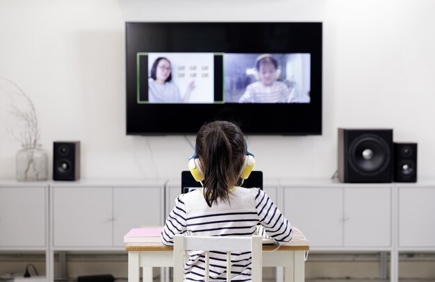 Asian schoolgirl learning at home with laptop computer using video call with her teacher, social distance during quarantine isolation during the Coronavirus (COVID-19) health care