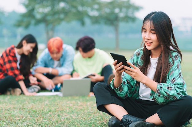 写真 友達のグループと一緒に公園で勉強しているアジアの女子学生