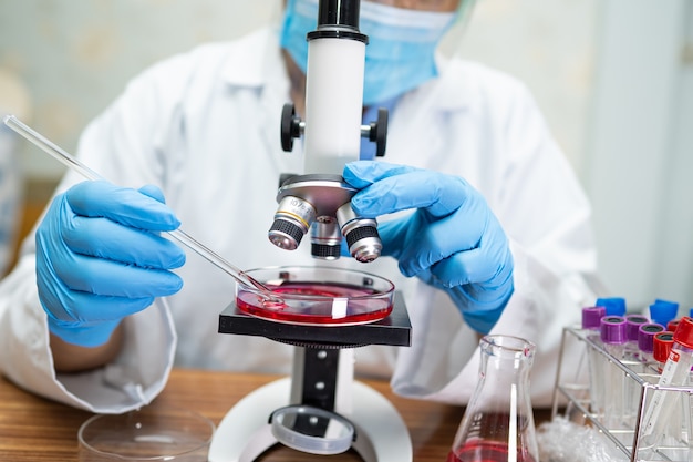 Asian scientist wearing mask working research with a microscope in laboratory.