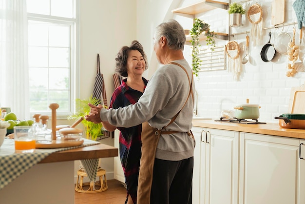 Asian senior adult couple cooking healthy food together at home while dancing in the kitchen morning weekendhappiness asian old marry couple enjoy romantic Cropped shot of a senior couple dancing