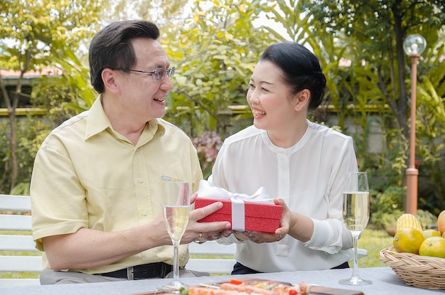 Asian senior couple smile happily enjoy at home and give gift\
boxes to live well after retirement