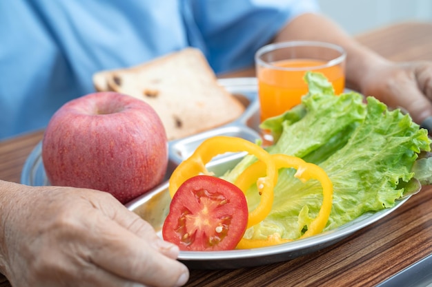 病院のベッドに座って空腹の間に希望と幸せで朝食野菜の健康食品を食べるアジアの高齢者または高齢の老婦人女性患者。