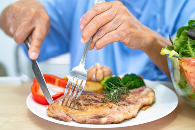 아시아 노인 또는 노인 여성 환자는 병원 침대에 앉아 배고픈 동안 희망과 행복으로 아침 식사와 야채 건강식을 먹고 있습니다.