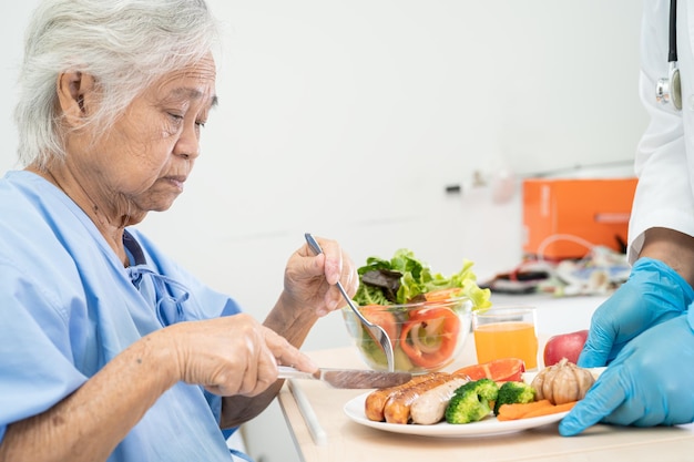 病院のベッドに座って空腹の間に希望と幸せを持って朝食と野菜の健康食品を食べるアジアの高齢者または高齢者の老婦人女性患者