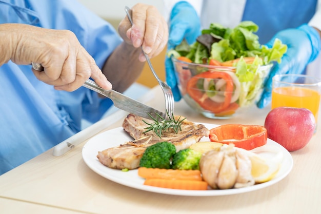 Азиатская пожилая или пожилая женщина-пациентка ест завтрак и овощную здоровую пищу с надеждой и радостью, сидя и голодная на кровати в больнице