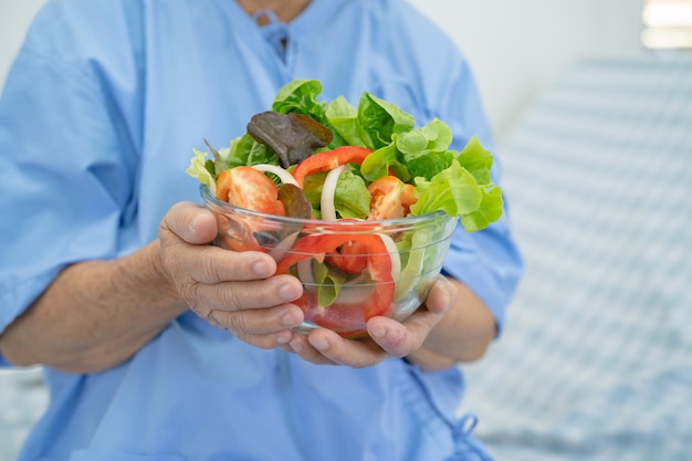 病院のベッドに座って空腹の間に希望と幸せで朝食野菜の健康食品を食べるアジアの高齢者または高齢者の老婦人女性患者