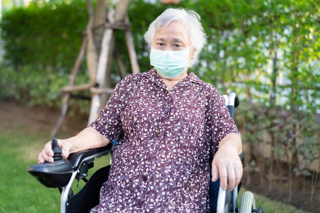 Asian senior or elderly old lady woman patient on electric wheelchair with remote control and wearing a face mask for protect safety infection Covid 19 Coronavirus