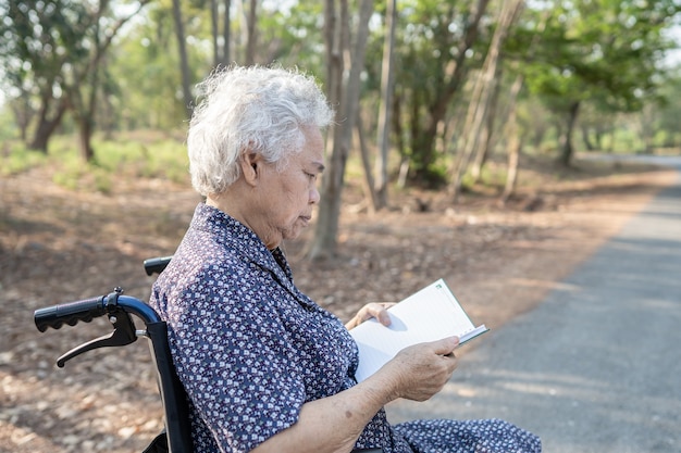 看護病棟のベッドに座って本を読んでいるアジアの高齢者または高齢の老婦人女性患者、健康的な強力な医療コンセプト。