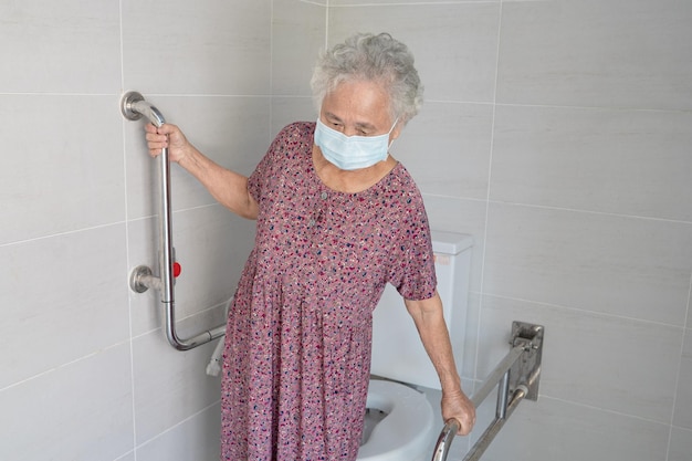 아시아 노인 또는 노인 여성 환자는 요양 병원 병동의 건강한 강한 의료 개념에서 화장실 화장실 손잡이 보안을 사용합니다.
