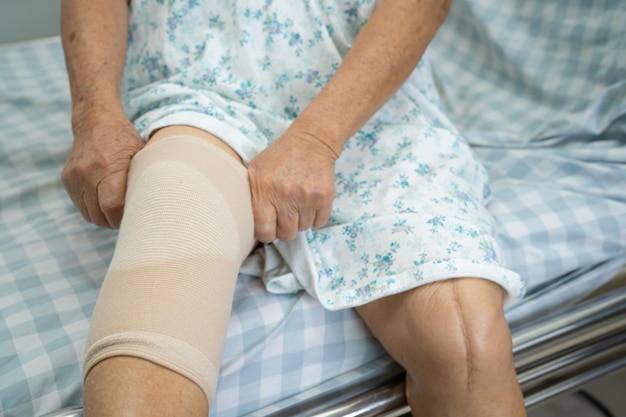 Asian senior or elderly old lady woman patient with knee support pain joint on bed in nursing hospital ward, healthy strong medical concept.