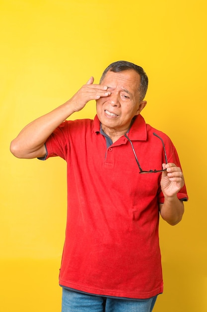 Asian senior man feels tired after reading with eye glasses isolated on yellow background Old man w