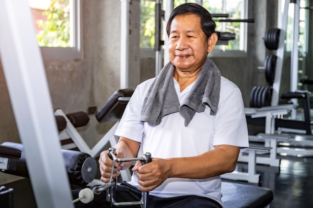 Asian senior man in sportswear training with machine at gym.