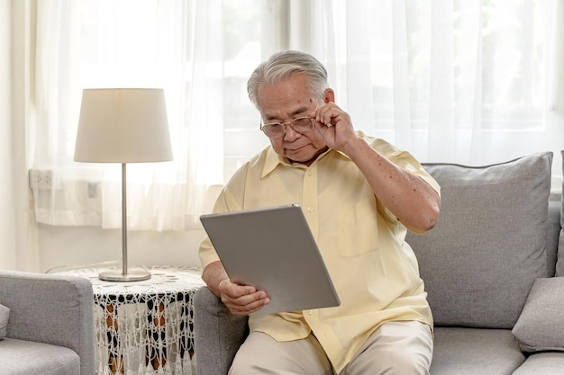 태블릿을 사용하고 은퇴 후 보험을 찾는 아시아 노인. 할아버지는 집에 혼자 있으세요.