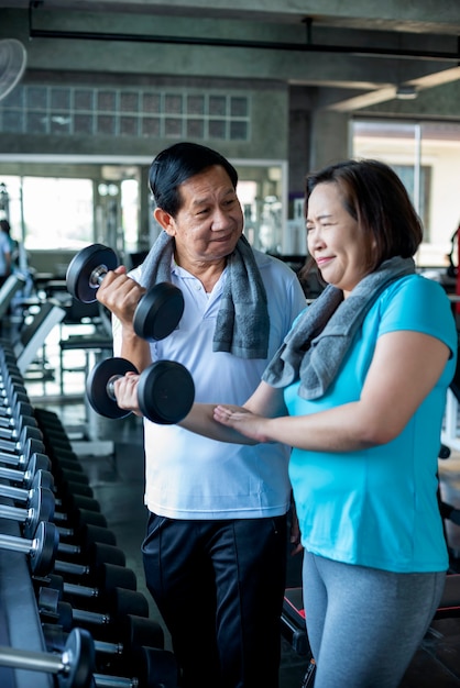 Asian senior man and woman exercise lifting dumbbell in fitness gym. elderly healthy lifestyle.