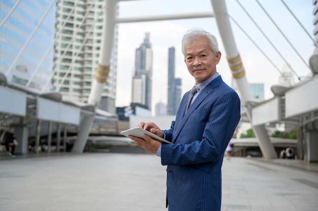 Asian senior mature middle aged businessman using tablet in modern city