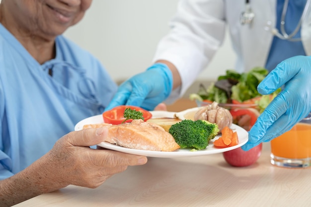 Asian senior old lady woman patient eating breakfast and vegetable healthy food with hope and happy while sitting and hungry on bed in hospital