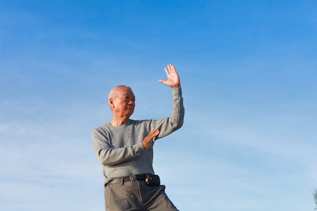 L'uomo anziano maggiore asiatico pratica il kungfu cinese di taichi sulla spiaggia