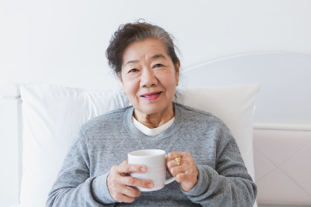 침대에서 커피 또는 차를 마시는 아시아 수석 늙은 여자