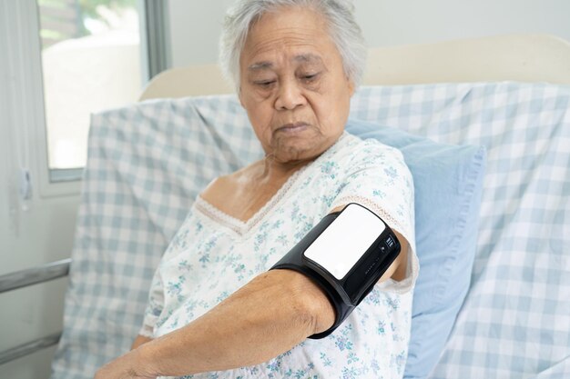 Asian senior old woman using wireless digital home measure blood pressure machine medical device to monitor heart health algorithm.