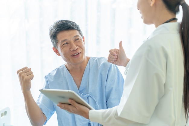 Asian senior patient on hospital bed discussing with female doctor