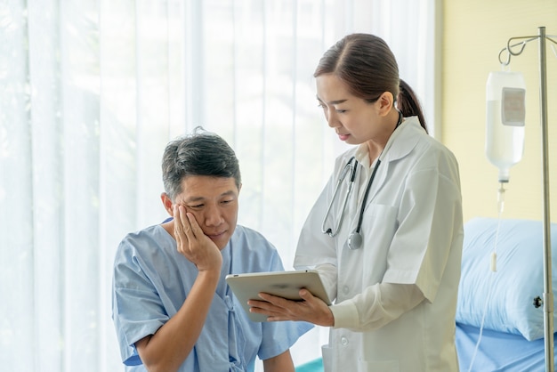 Азиатский старший пациент на больничной койке обсуждая с женским доктором