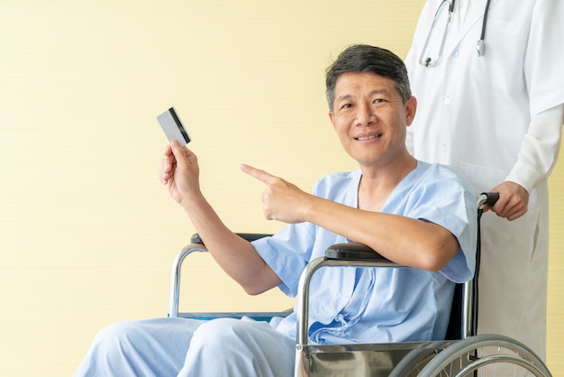 Азиатская старшая терпеливая кресло-коляска усмехаясь с кредитной карточкой