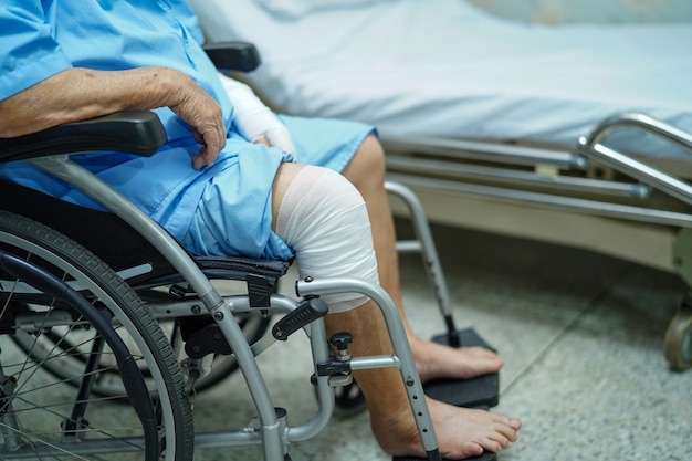 Asian senior woman patient accident at knee with bandage on wheelchair in hospital.