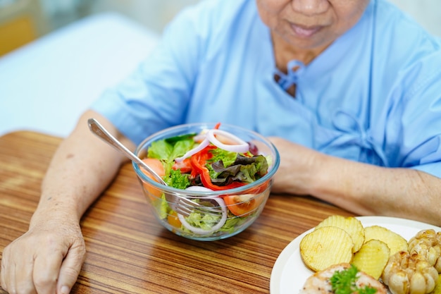 アジアの年配の女性患者が病院で朝食を食べる。