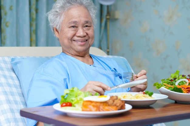 Азиатский старший пациент женщины есть завтрак в больнице.