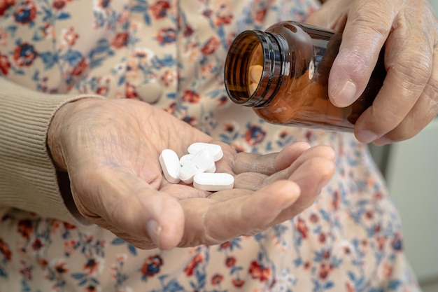 Азиатская пожилая женщина-пациентка держит капсульные таблетки с антибиотиками для лечения пациента с инфекцией в больнице. Концепция аптеки