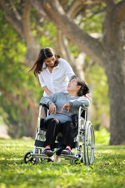 Asian senior woman sitting on the wheelchair with her daugther family happy smile face on the green park