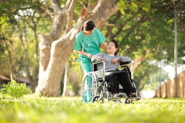 Asian senior woman sitting on the wheelchair  with woman in doctor uniform in the park hospital