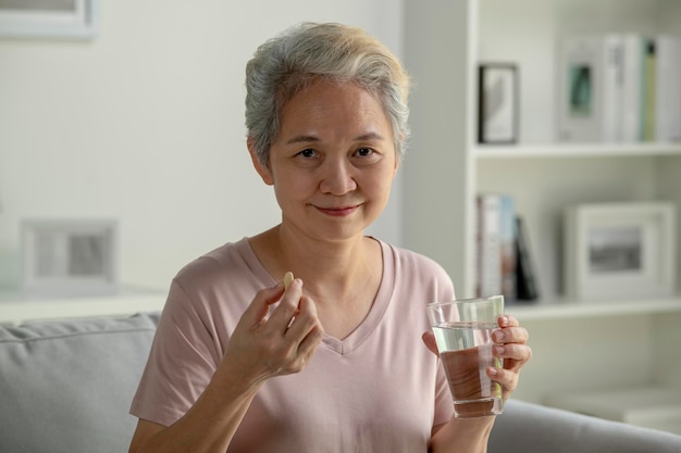 Asian senior woman taking medicine at home smiling and looking at camera