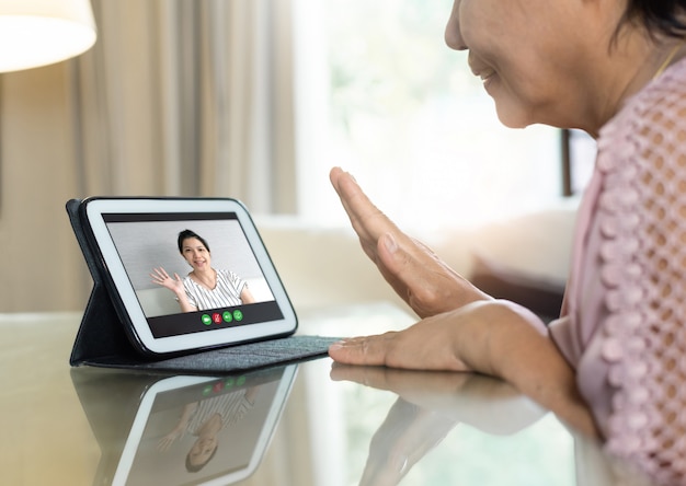 Asian Senior woman waving hand and talking to her relatives and family via internet and wireless technology.