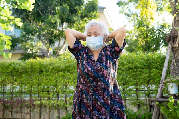 マスクを持つアジアの年配の女性は、公園で幸せ、健康的な強力な医療コンセプトでコロナウイルスの運動を保護します