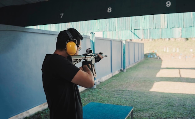 写真 ノイズ キャンセリング ヘッドフォンと黒い服を着て射撃場で射撃ライフルを練習しているアジアの射手男 瞑想と自衛のレクリエーション活動のための射撃スポーツ