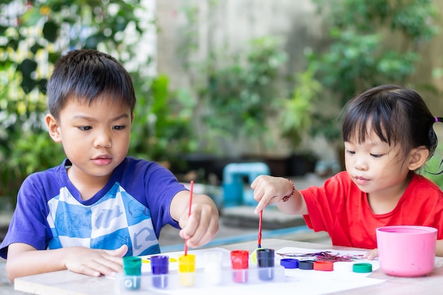 Asian sibling children drawing and painting colours on the paper in the room.