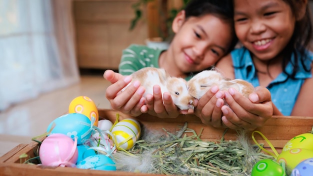 Asian siblings children are playing with baby bunny and\
decorating easter eggs preparing for easter at home together with\
fun happy family happy easter happy holiday