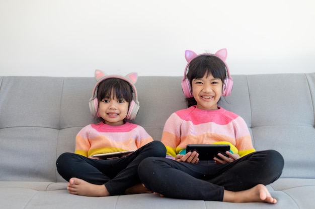 Азиатская девочка-братья и сестры просматривают социальные сети и играют на смартфоне и цифровом планшете, обучаются онлайн дома
