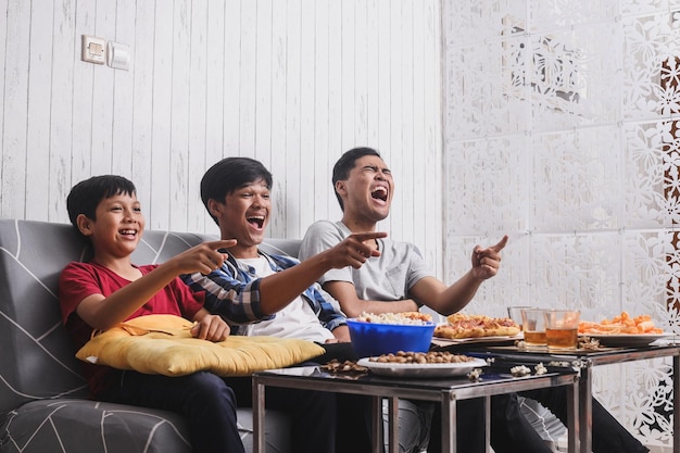 Asian siblings laugh out loud while watching funny movie on TV at home