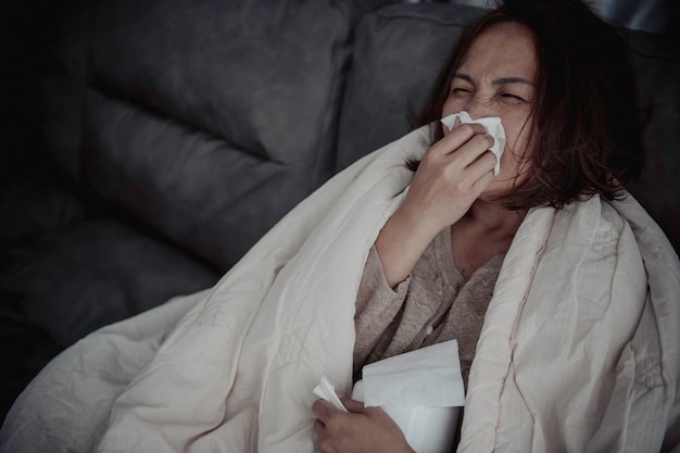 Asian sick woman sit on the sofa stay at homethe woman felt bad\
wanted to lie down and resthigh fever